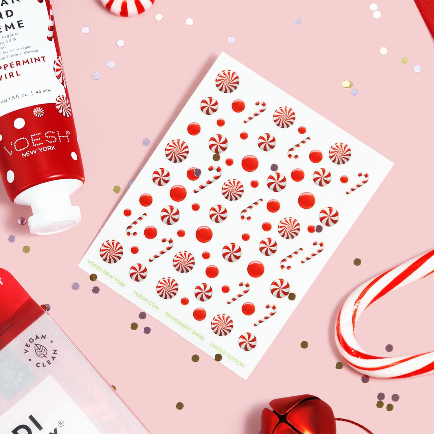 One sheet of Peppermint Swirl Nail Art Stickers next to Peppermint Swirl Vegan Hand Crème on a pink background with confetti, bells, and candy canes.